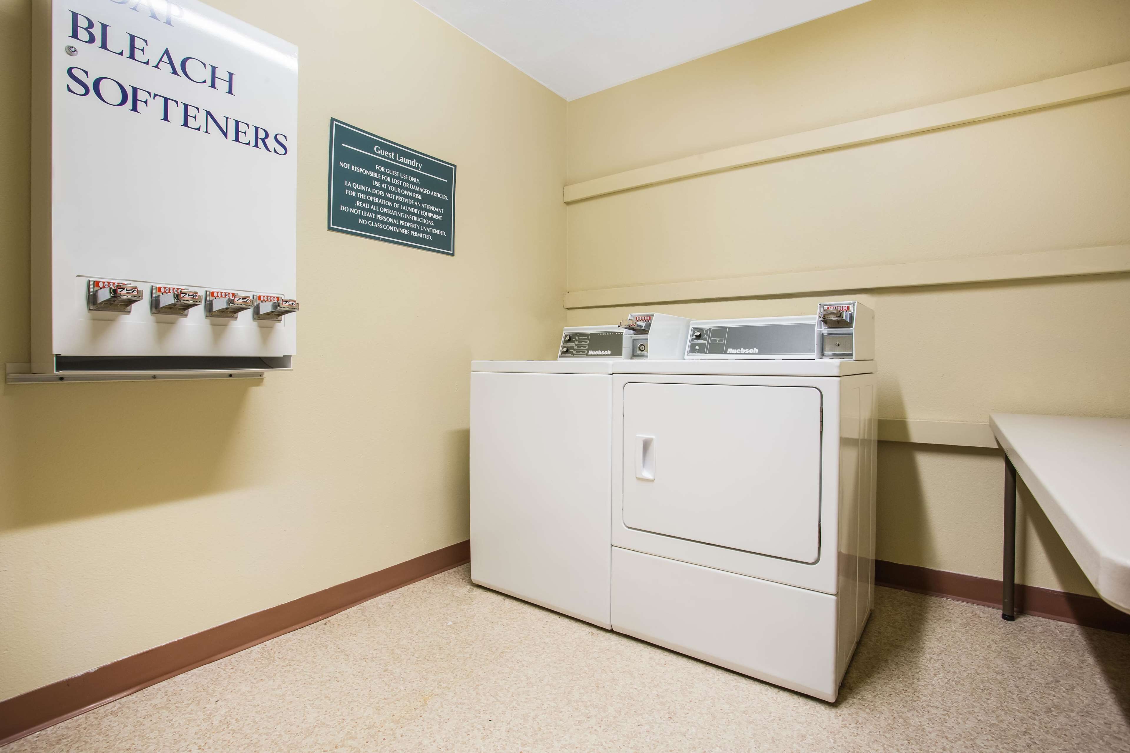 A laundry room with a washer and dryer, a sign for bleach and softeners, and a caution sign for the laundry area.