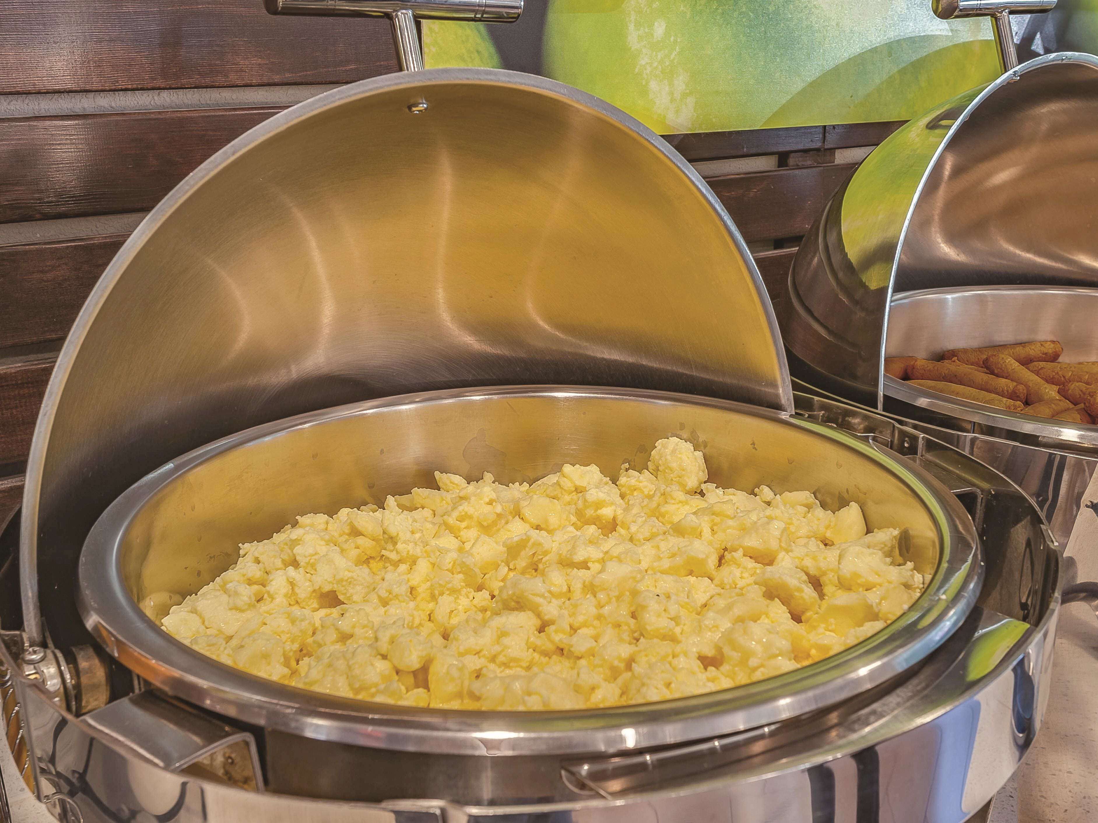 Un bufé con huevos revueltos y alimentos fritos.