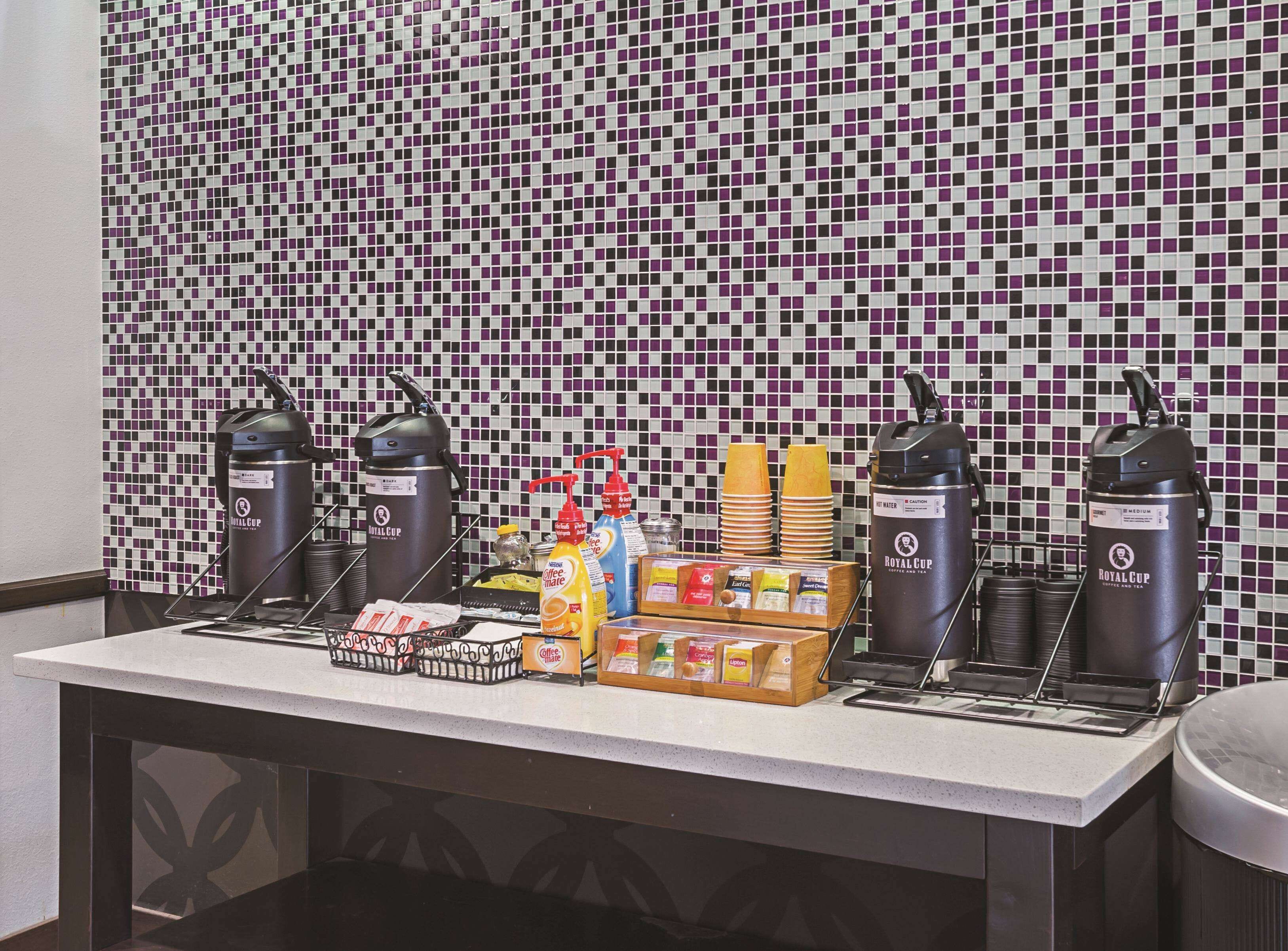 Una estación de café con varias máquinas de café Royal Cup, vasos desechables y una variedad de productos de café y té.
