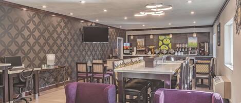 A modern cafe with purple chairs, a bar area, and a flat-screen TV on the wall.