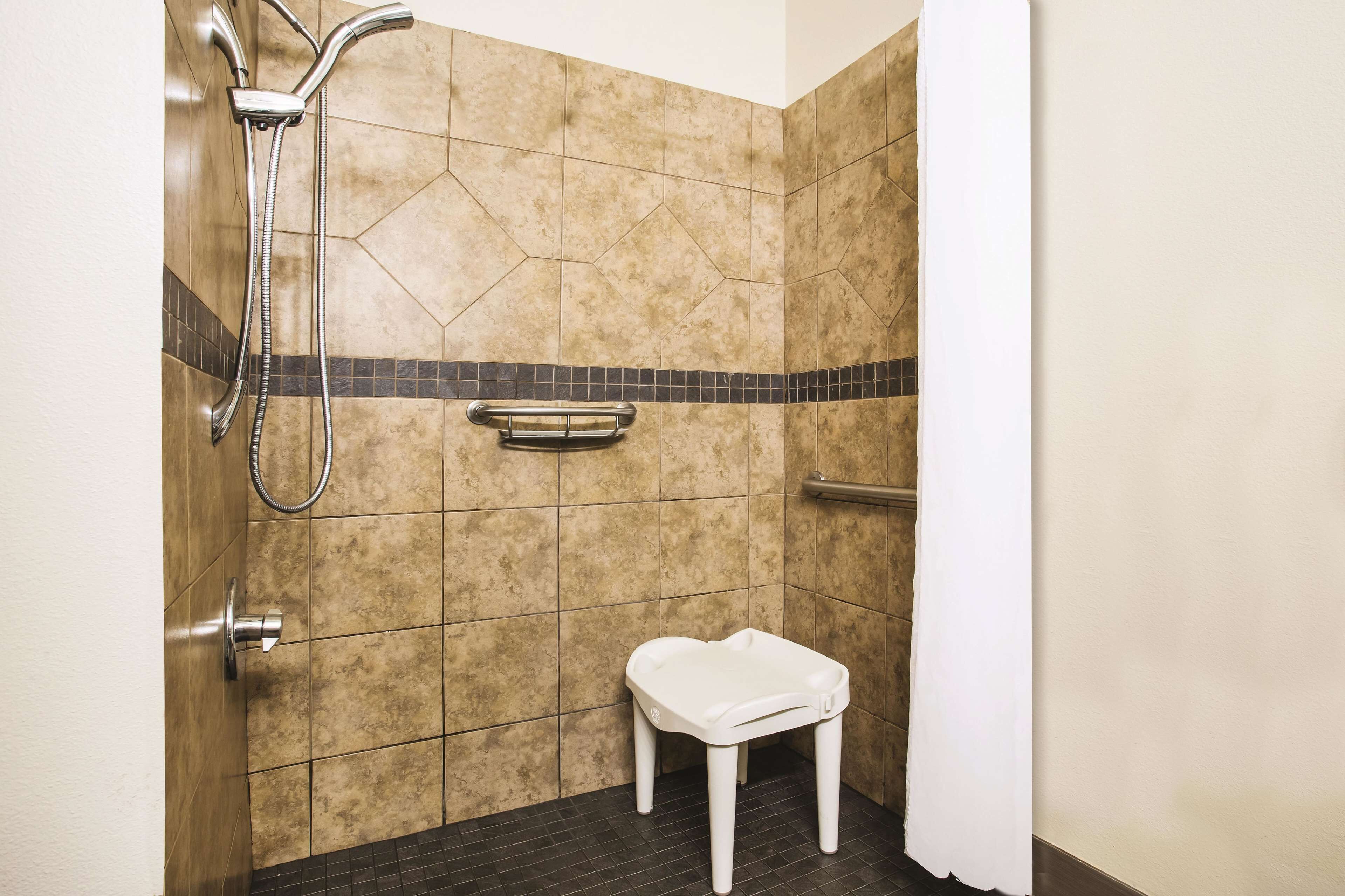 A small, tiled shower area with a white bench, a handheld showerhead, and a towel rack.