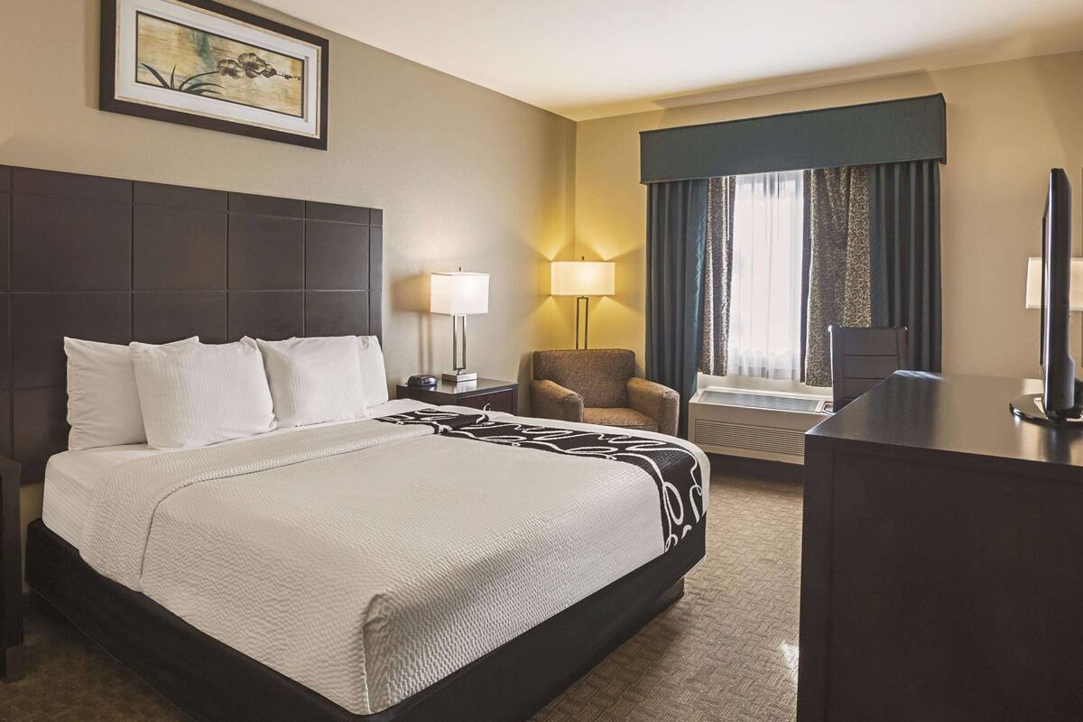 Een hotelkamer met een groot bed, twee nachtkastjes, een stoel, een bureau, een televisie en een raam met gordijnen.