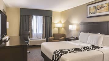A hotel room with a large bed, two bedside tables with lamps, a desk with a TV, a chair, and a window with curtains.