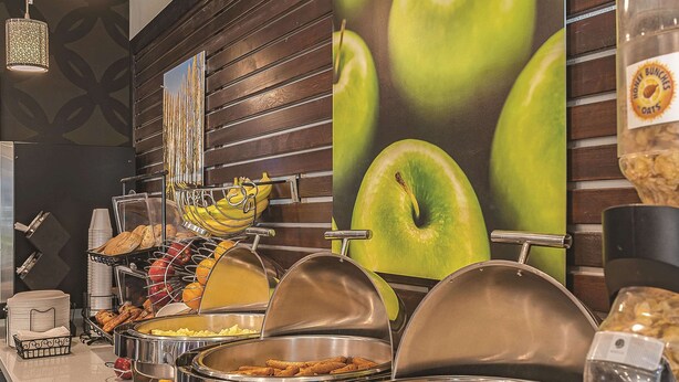 A buffet area with various food items, including fruits, pastries, and a large wall with a fruit-themed mural.