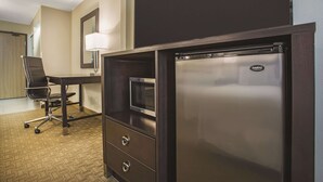 A hotel room with a desk, chair, built-in microwave, and refrigerator.