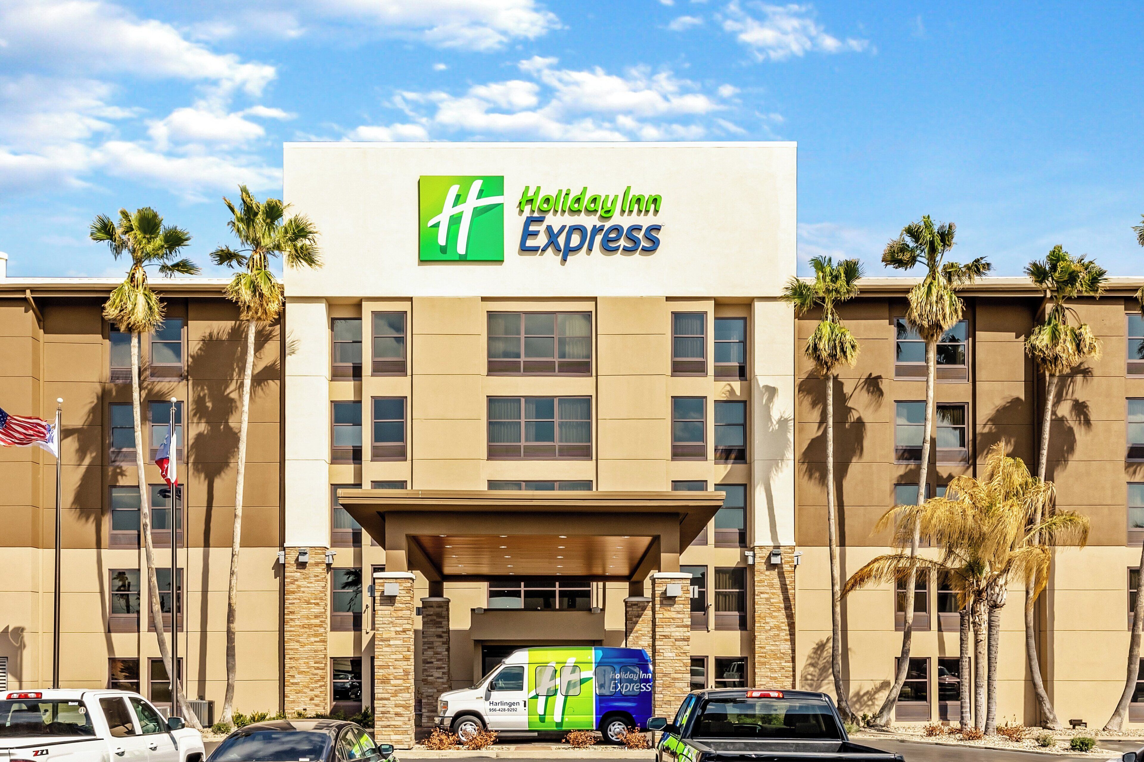 A Holiday Inn Express building with a clear sky, palm trees, and a parking lot with vehicles.