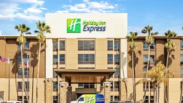 A Holiday Inn Express building with a clear sky, palm trees, and a parking lot with vehicles.