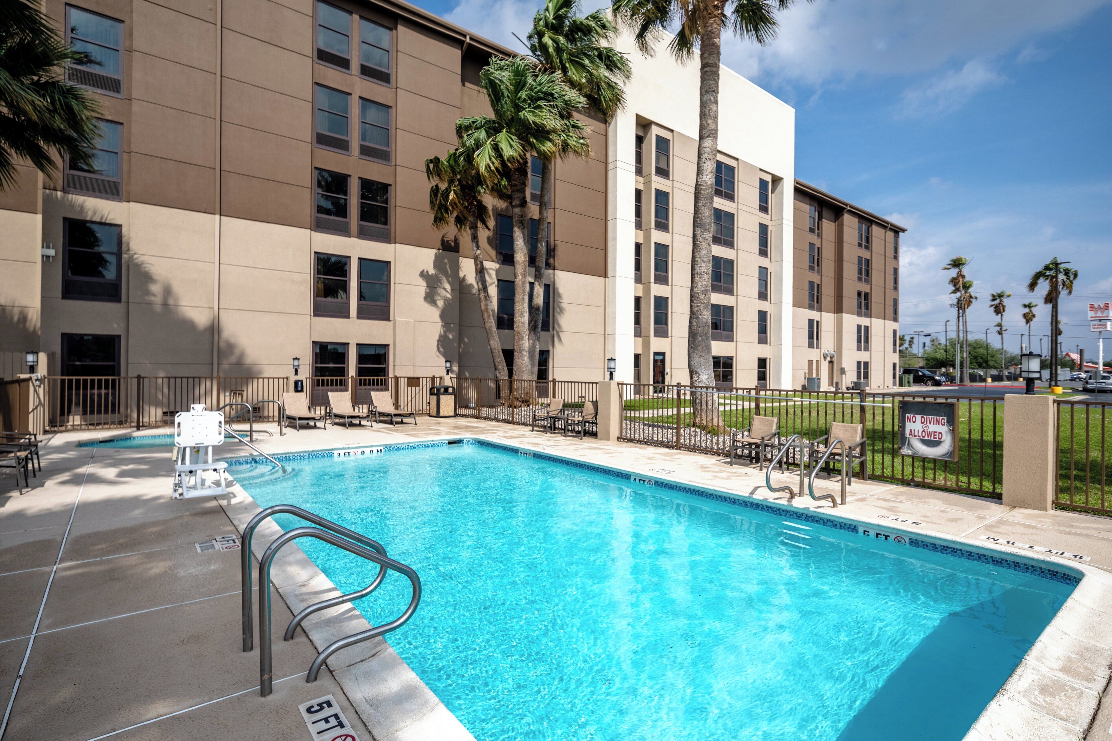 A swimming pool with a 5 ft depth marker, surrounded by a fence, with a building in the background.