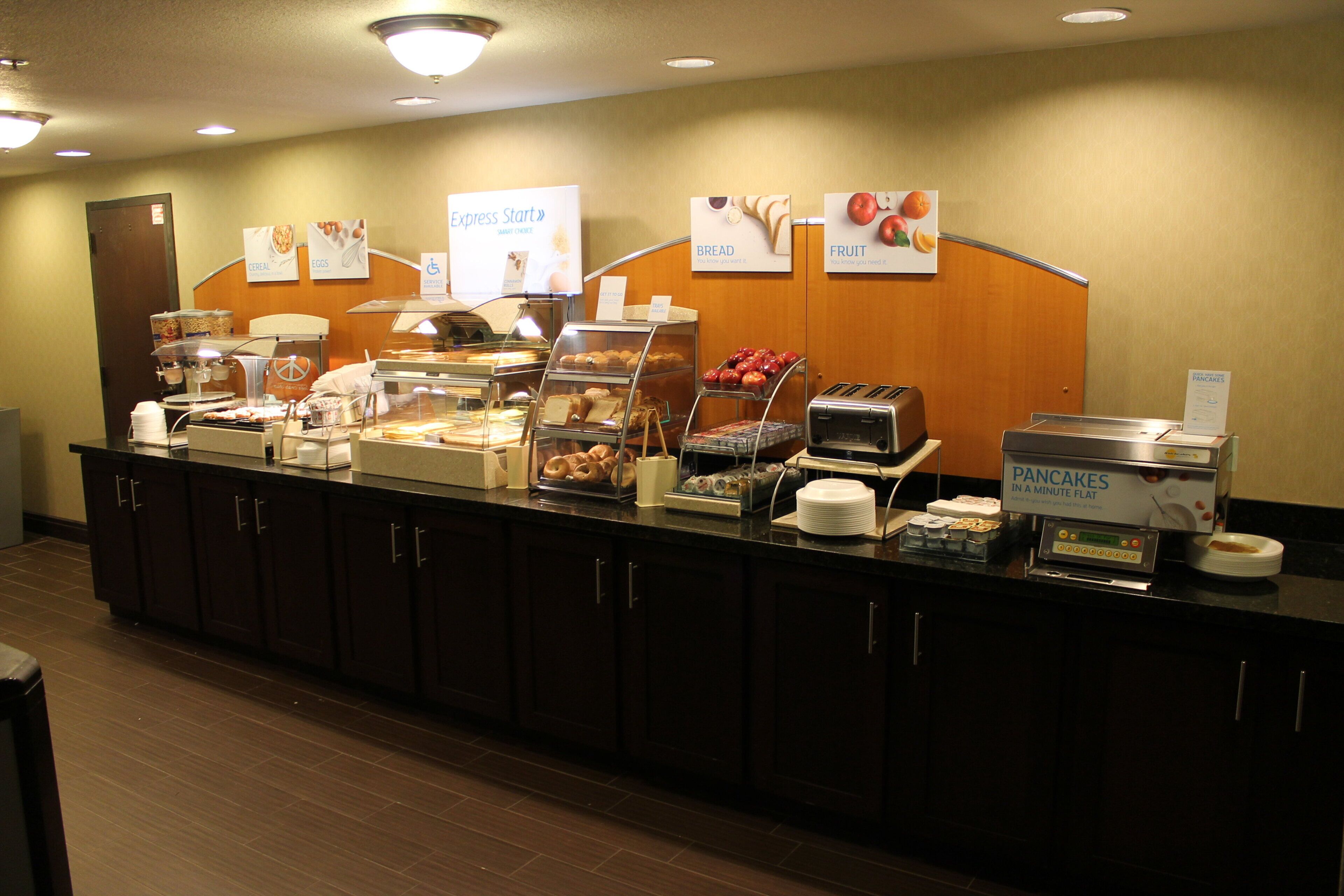 A self-service breakfast station with various food options and a sign indicating the availability of pancakes.