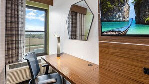A hotel room with a wooden desk, a chair, a large window with curtains, a wall-mounted mirror, and a view of a boat on a turquoise sea. - Holiday Inn Express Harlingen by IHG (Harlingen)