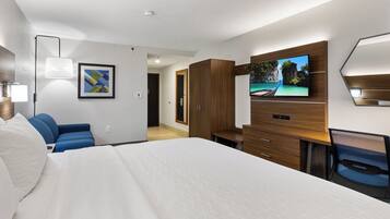 A hotel room with a large bed, a TV mounted on the wall, a desk, and a blue chair.