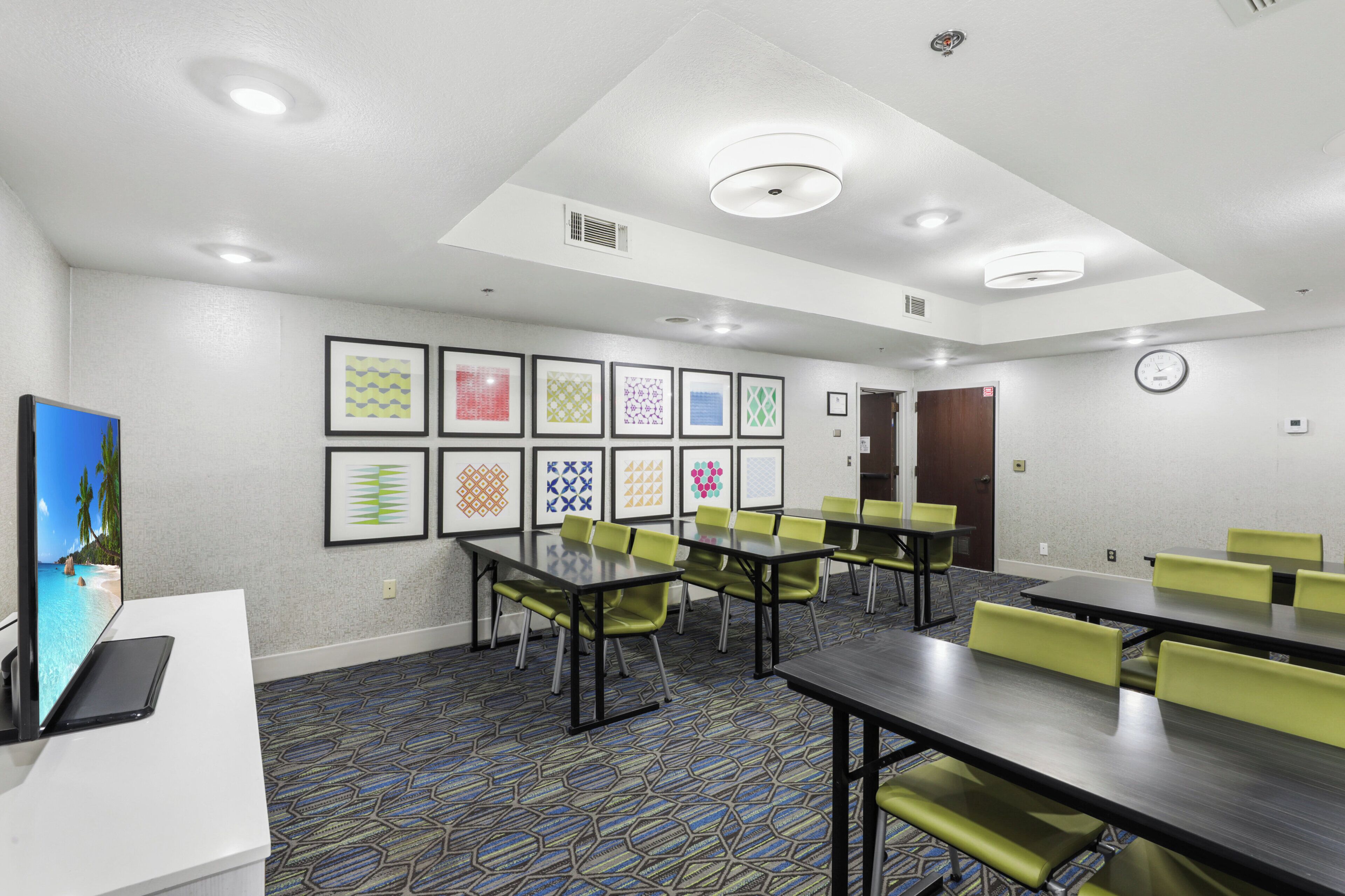 A conference room with tables and chairs, a clock, and framed artwork on the wall.