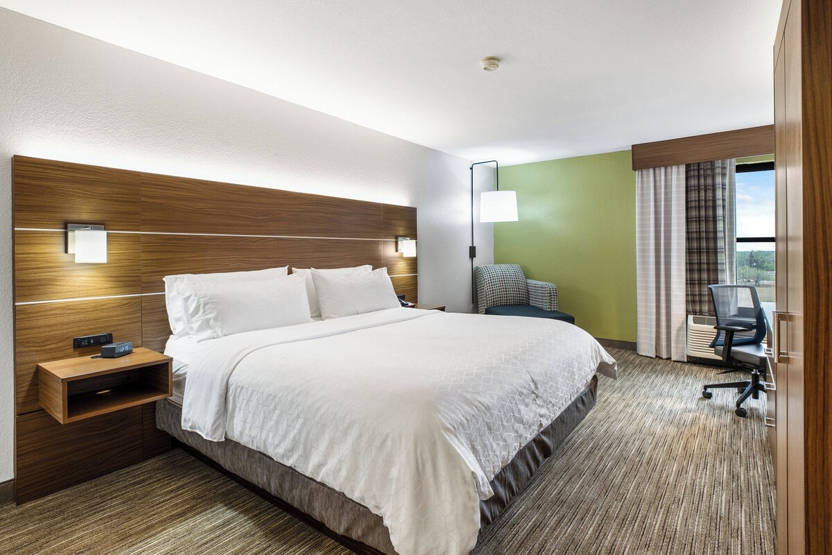 A hotel room with a large bed, bedside tables, a desk with a chair, and a view of the outdoors.