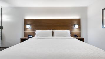 A modern hotel room with a large bed, wooden headboard, two bedside tables with lamps, and a simple, clean design.