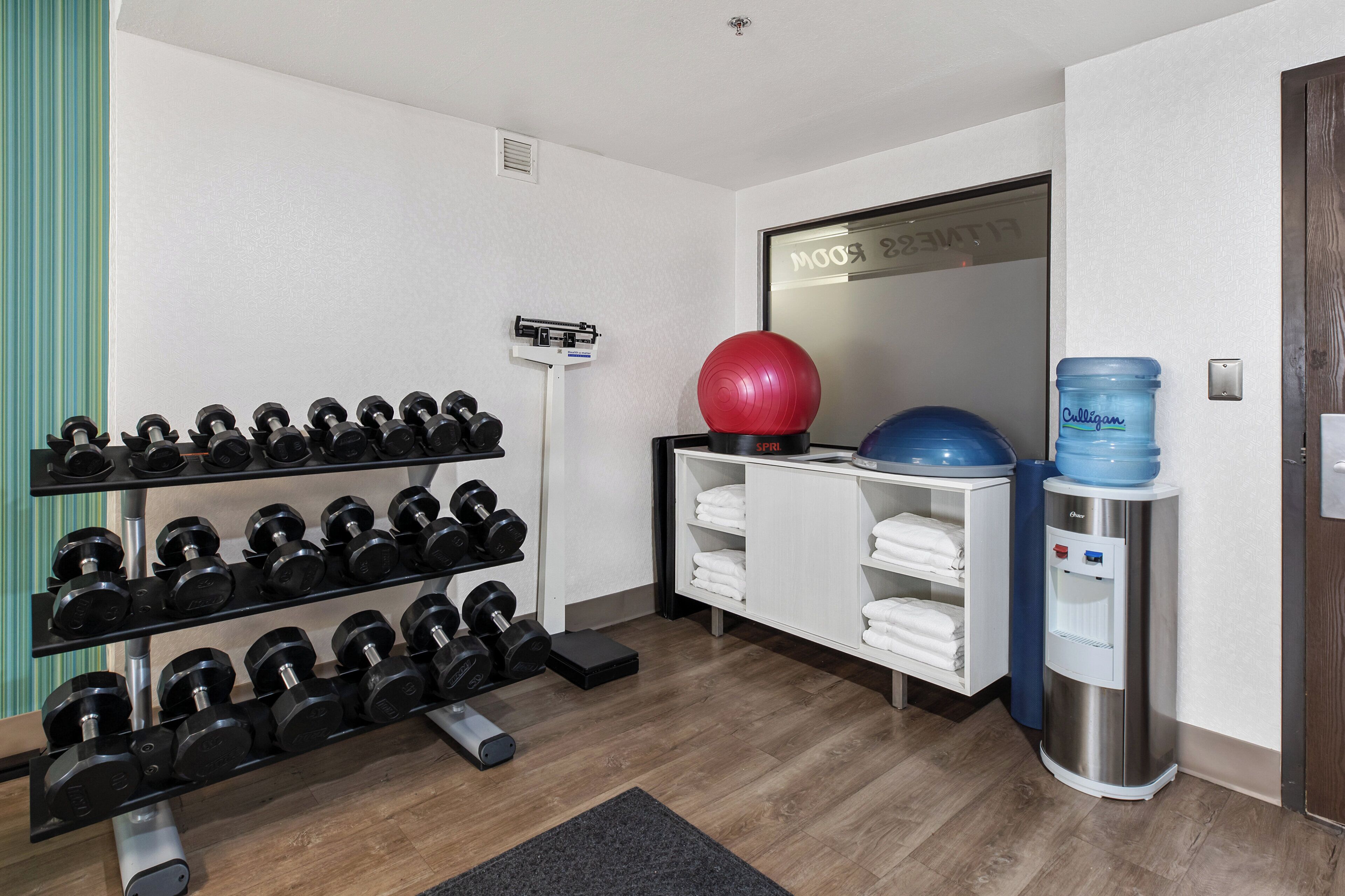 A gym with a rack of dumbbells, a red exercise ball, a water dispenser, and a mirror with a reflection.