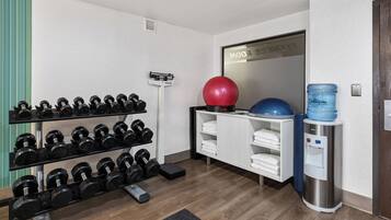 A gym with a rack of dumbbells, a red exercise ball, a water dispenser, and a mirror with a reflection.