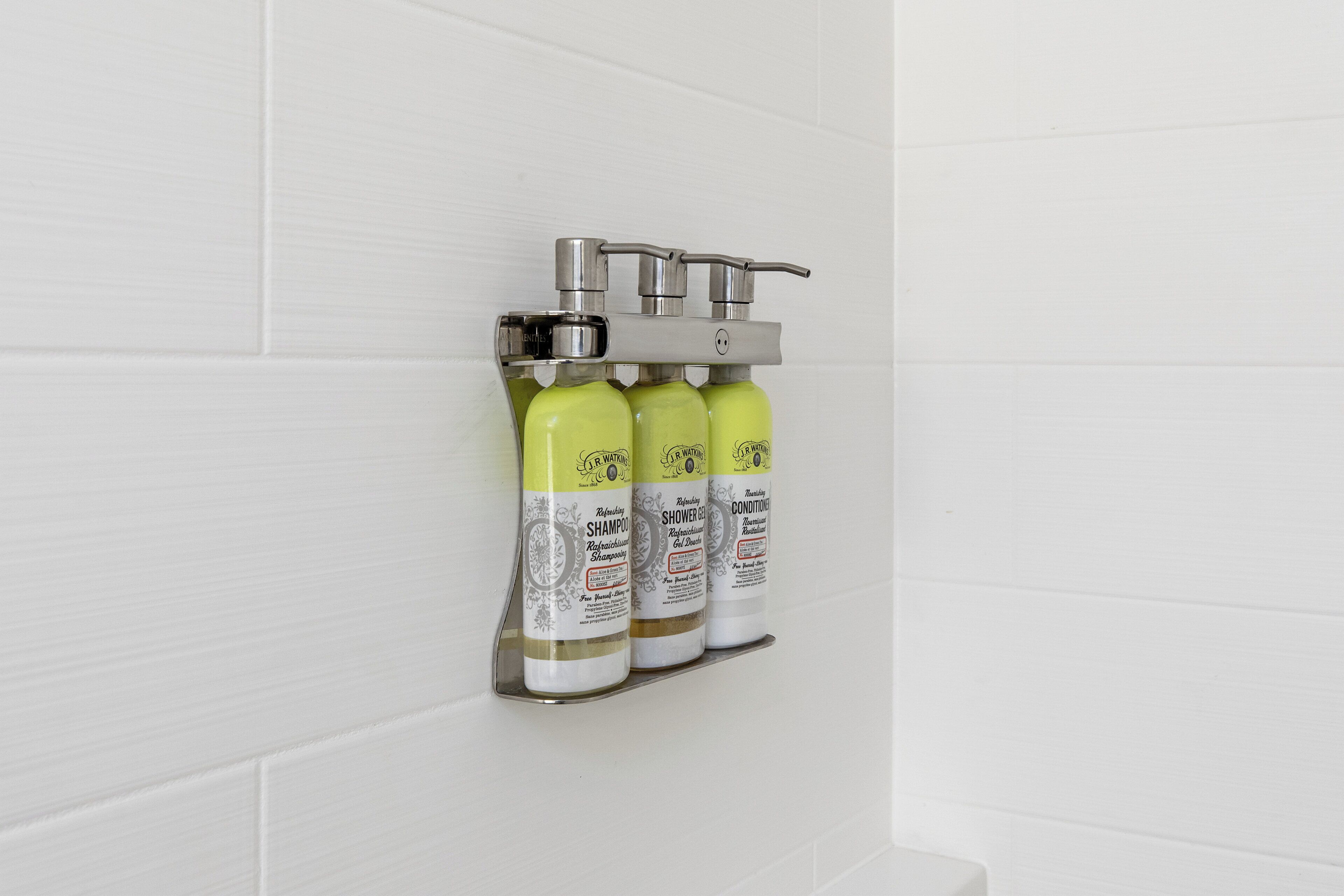 Un dispensador montado en la pared con tres botellas de gel de ducha J.R. Watkins.