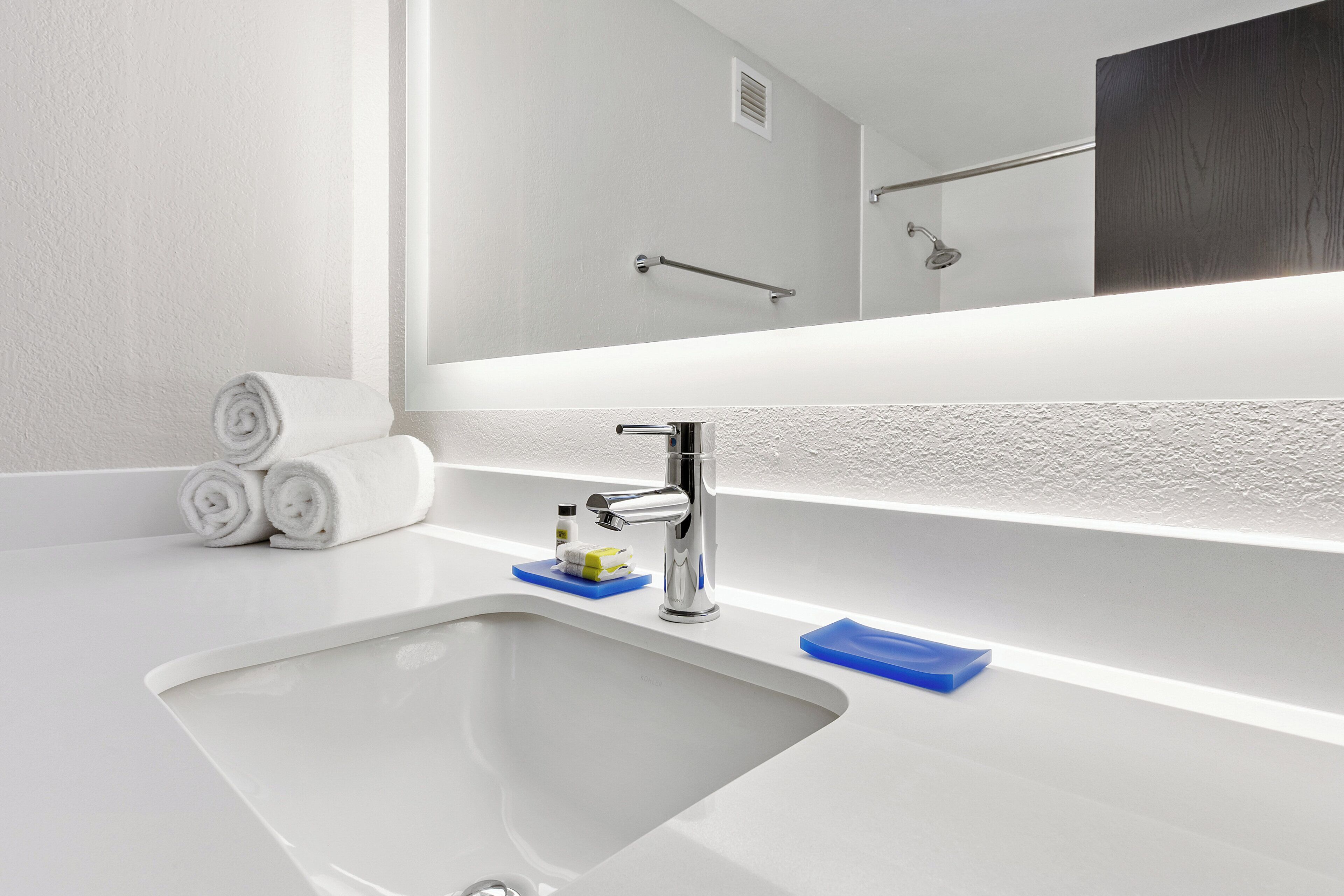 Un baño con lavamanos blanco, espejo y toallero.