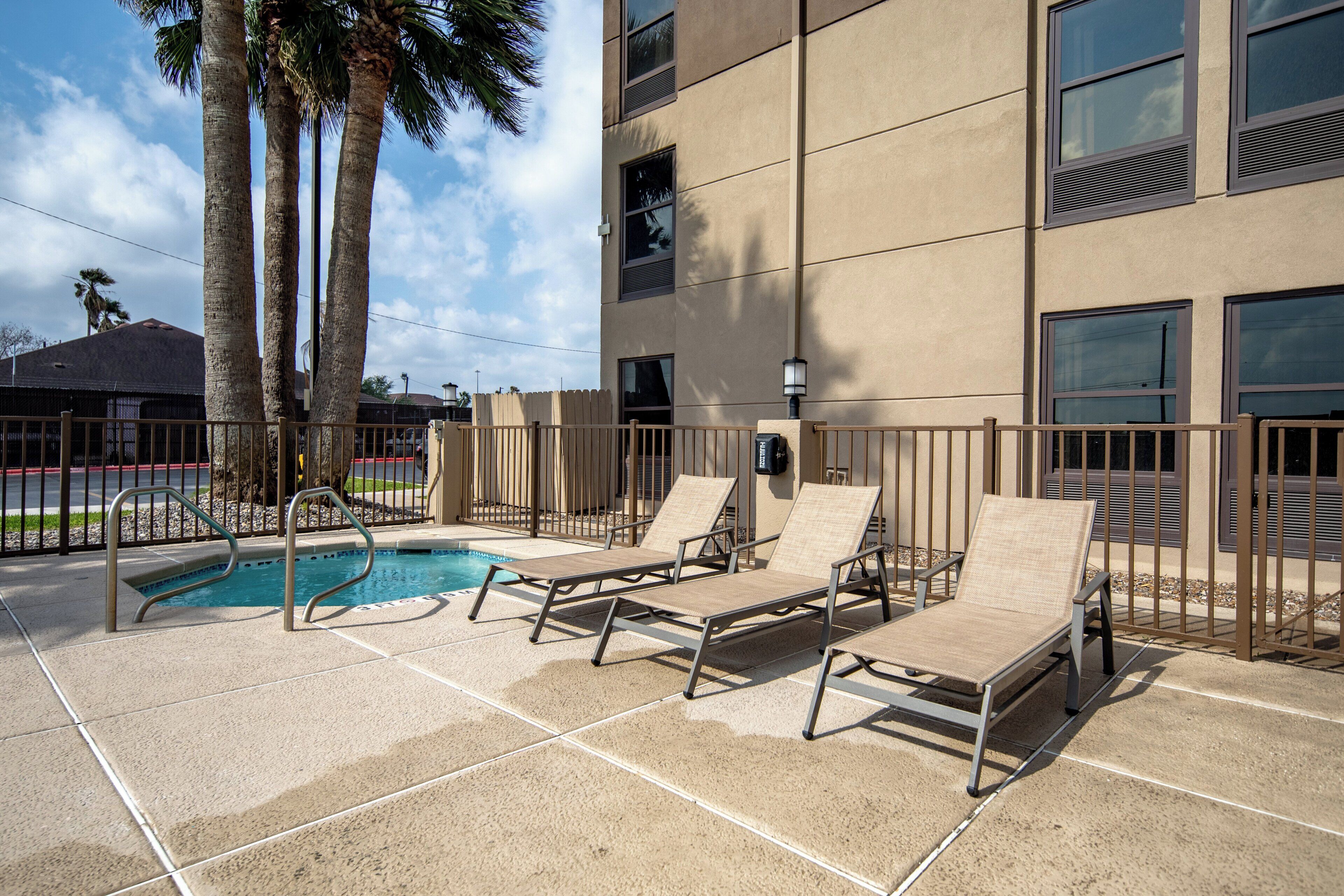 A pool area with lounge chairs and a fence.