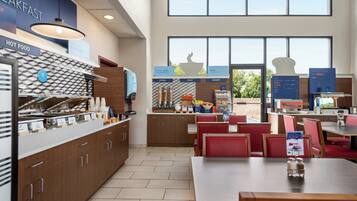 A breakfast area with a self-serve station, seating, and a view of the outdoors.
