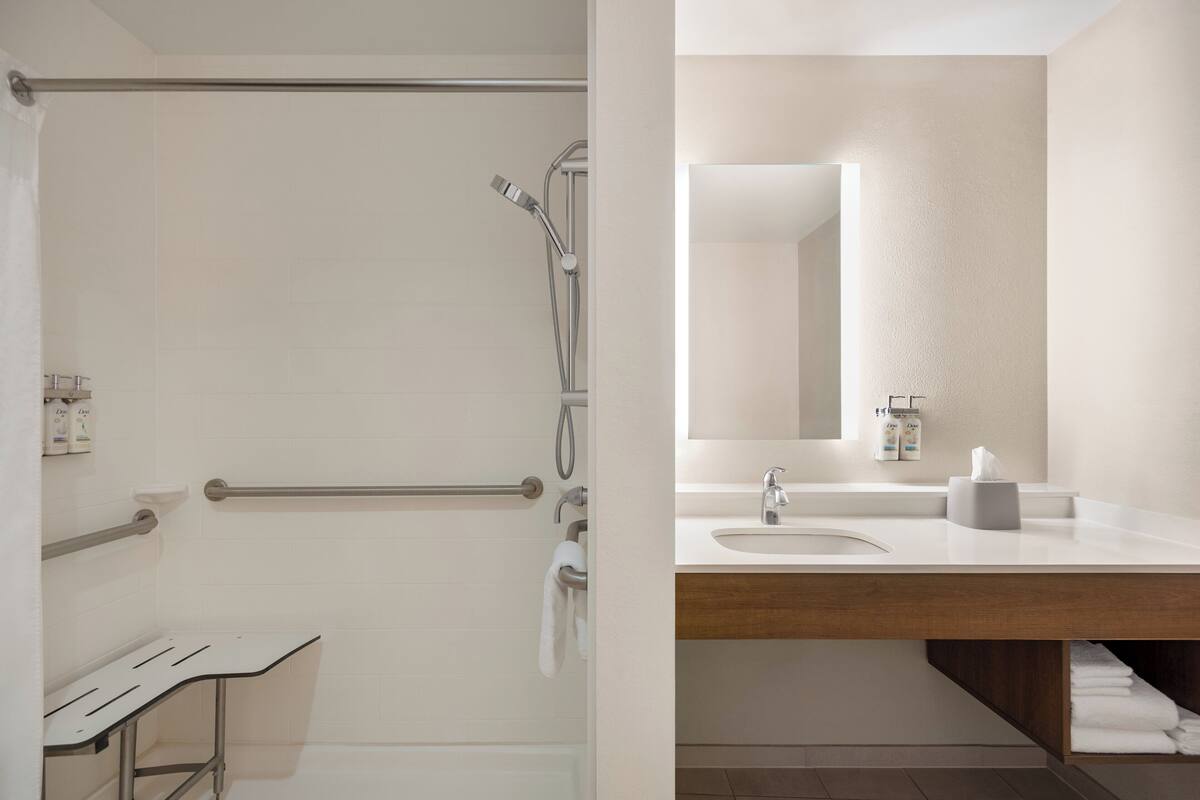 Ein Badezimmer mit Dusche, Haltegriffen, Waschbecken und Spiegel.