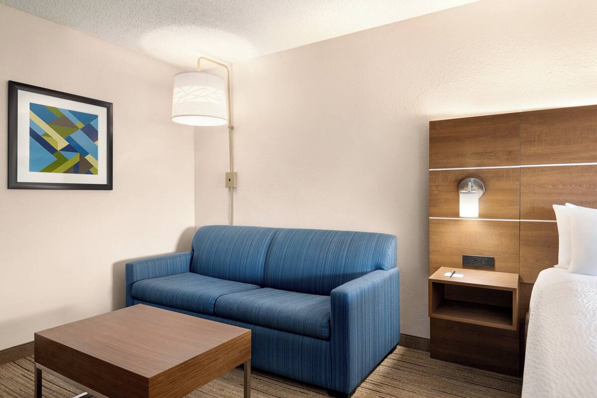 Ein Hotelzimmer mit einem blauen Sofa, einem Holztisch, einem Nachttisch und einem Bett.
