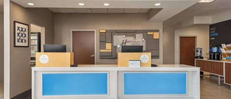 A hotel reception desk with a blue accent, a Holiday Inn Express sign, and a coffee station.