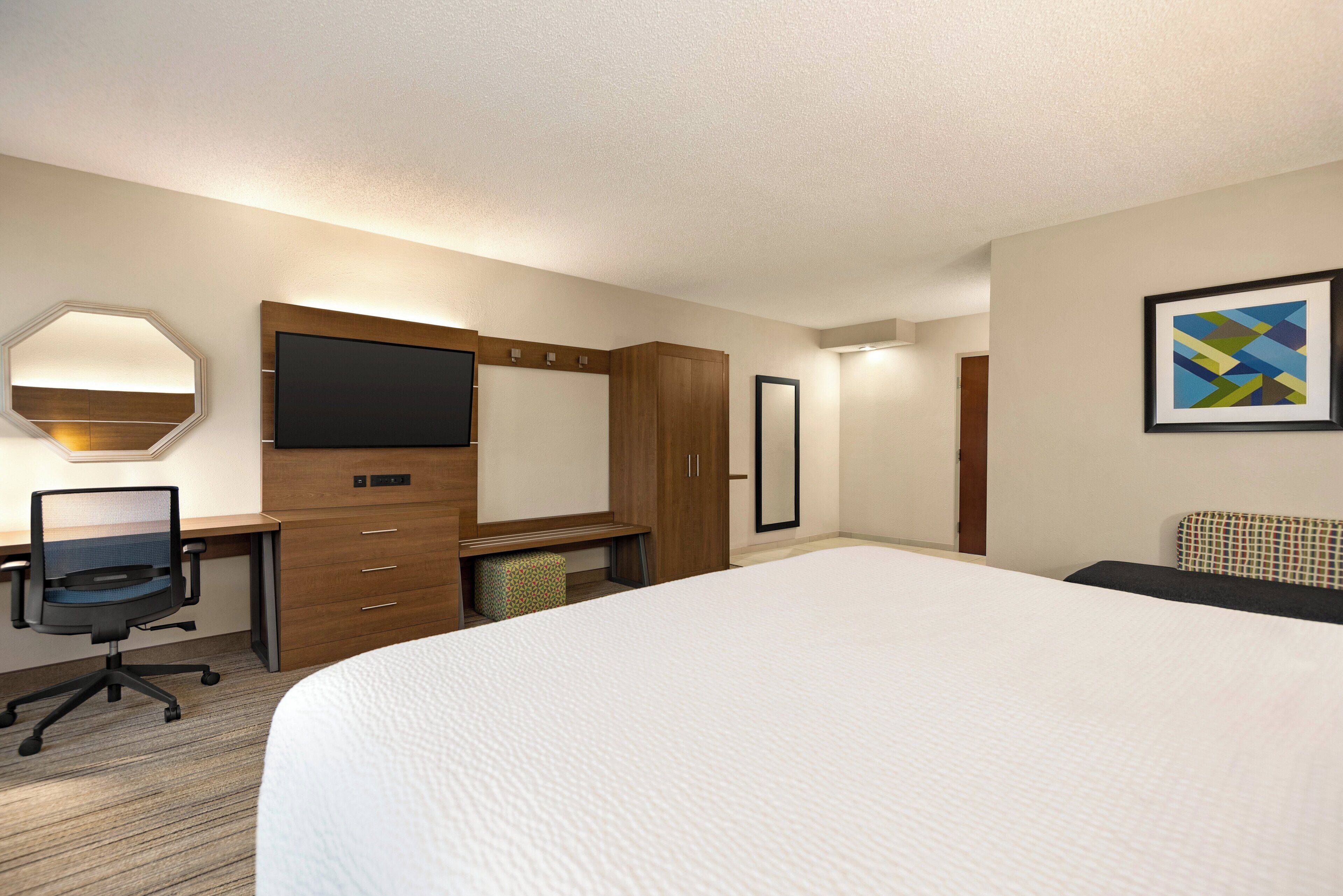 A hotel room with a large bed, a desk with a computer, a TV, and a wardrobe.