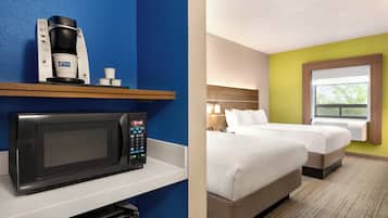A hotel room with a microwave, coffee maker, and a bed with two pillows.
