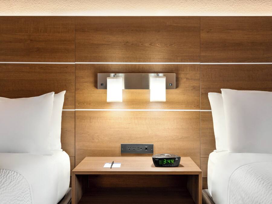Een hotelkamer met twee bedden, een nachtkastje, een spiegel en een digitale klok.