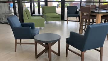 Una zona de estar con sillas y una mesa redonda, ventanas amplias con vistas al exterior, y una pared de ladrillo.
