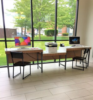 A workspace with two desks, chairs, a computer, a printer, and a window with a view of a green landscape and buildings. - Holiday Inn Express Winchester South-Stephens City by IHG (Stephens City)