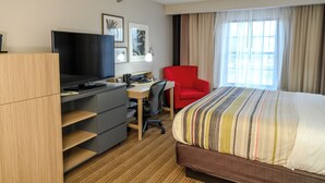 A hotel room with a bed, a desk with a computer, a TV, and a red chair.