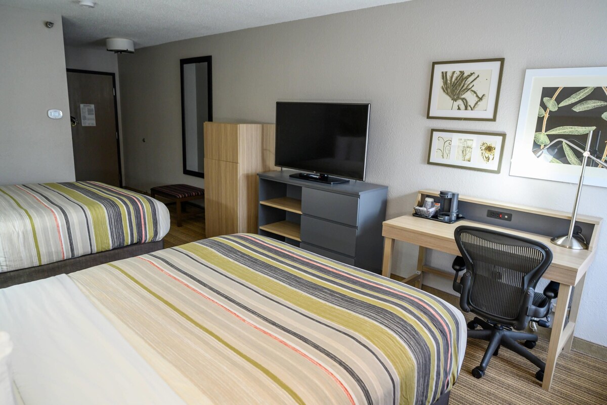 A hotel room with two beds, a desk with a computer, a television, and artwork on the wall.