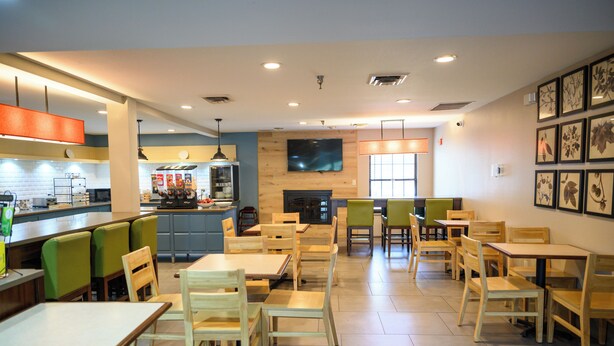 A restaurant with multiple dining tables and chairs, a kitchen area, and a television mounted on the wall.