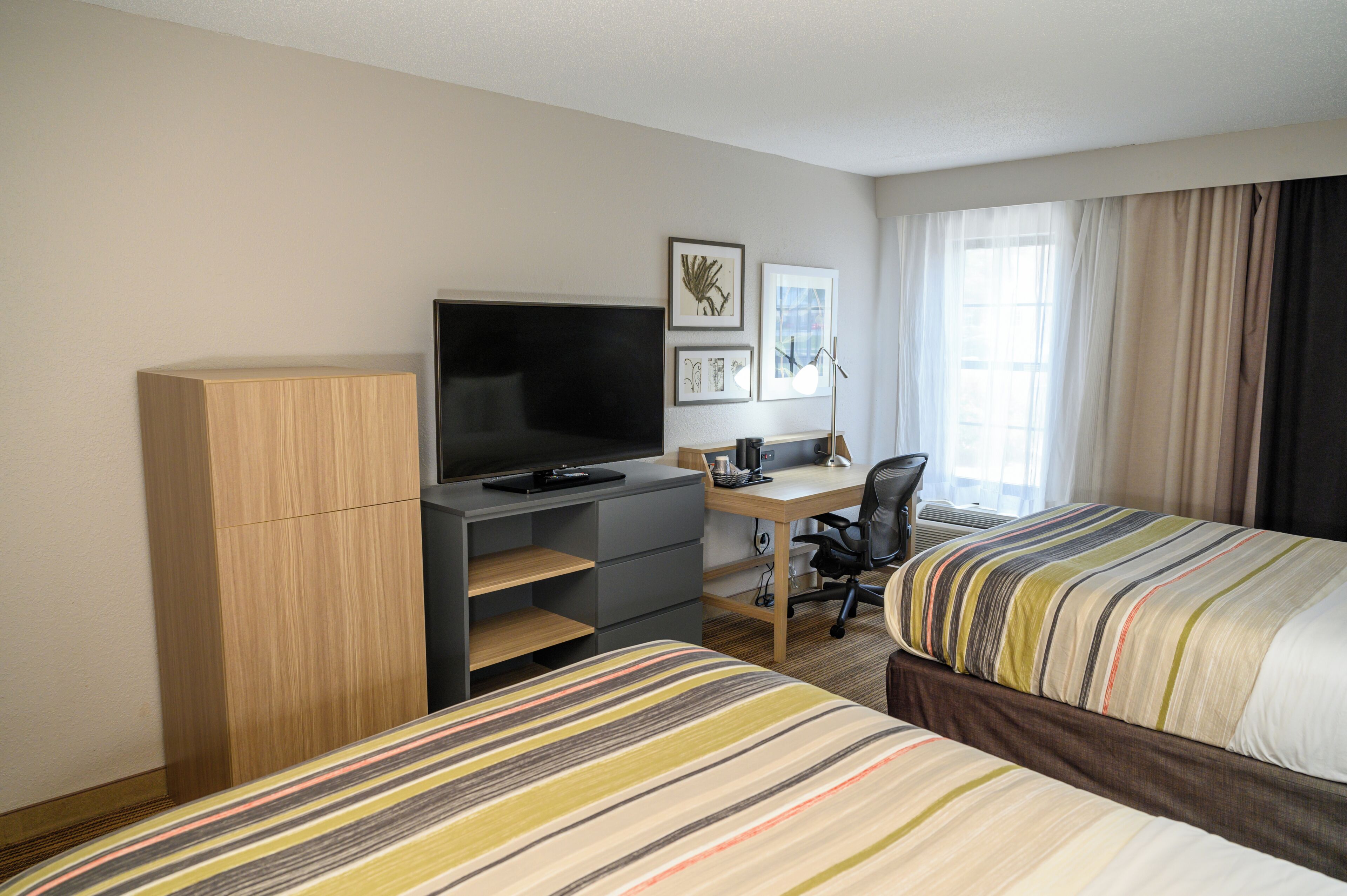 A hotel room with two beds, a desk with a computer, a television, and a wardrobe.
