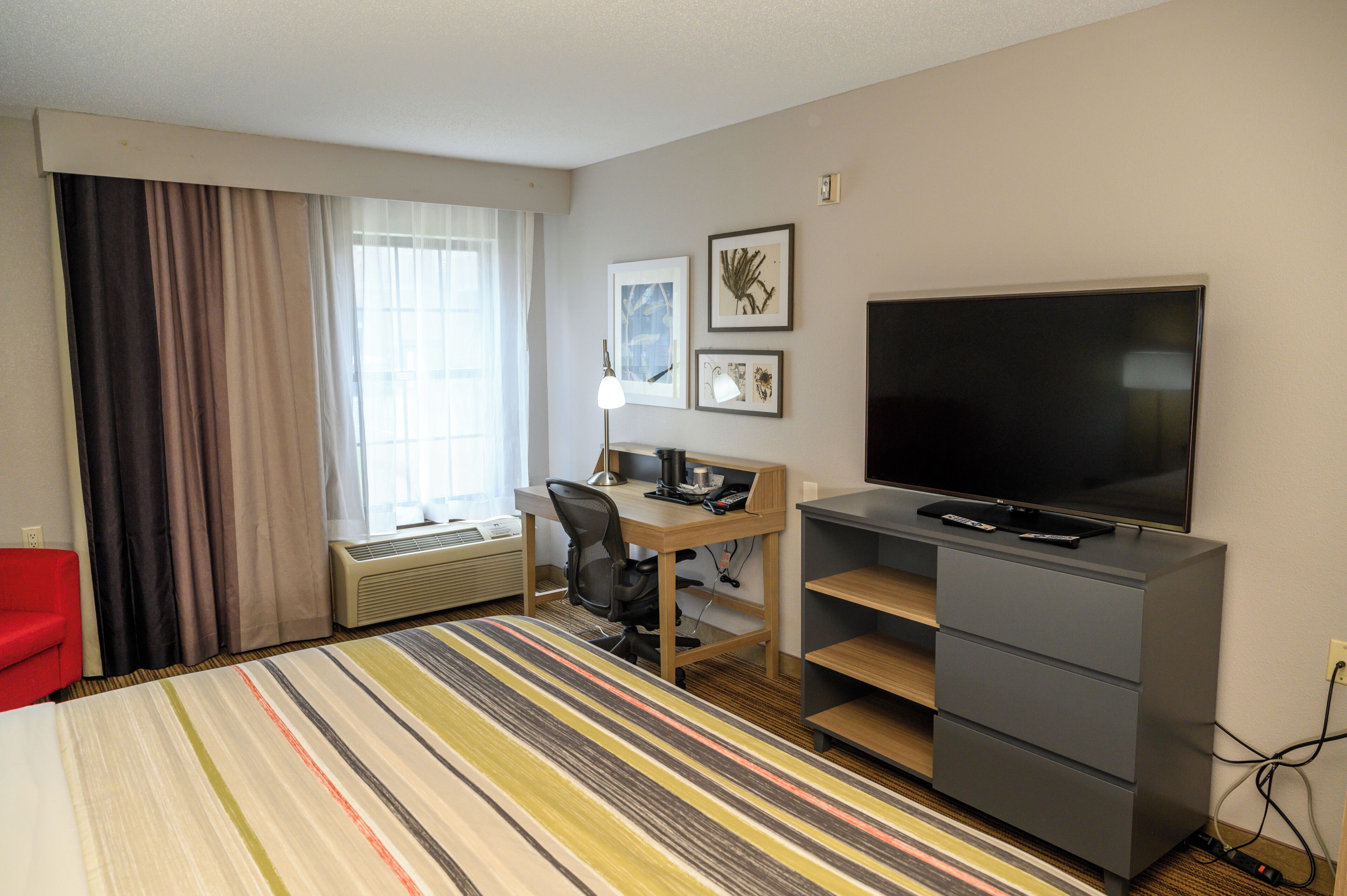 A hotel room with a bed, a desk with a chair, a television, and a window with curtains.