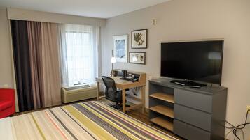 A hotel room with a bed, a desk with a chair, a television, and a window with curtains.
