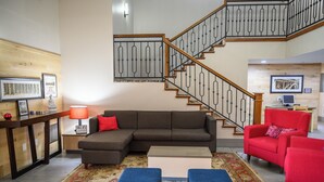 A living room with a sectional sofa, a red armchair, a coffee table, a patterned rug, and a staircase with a railing.