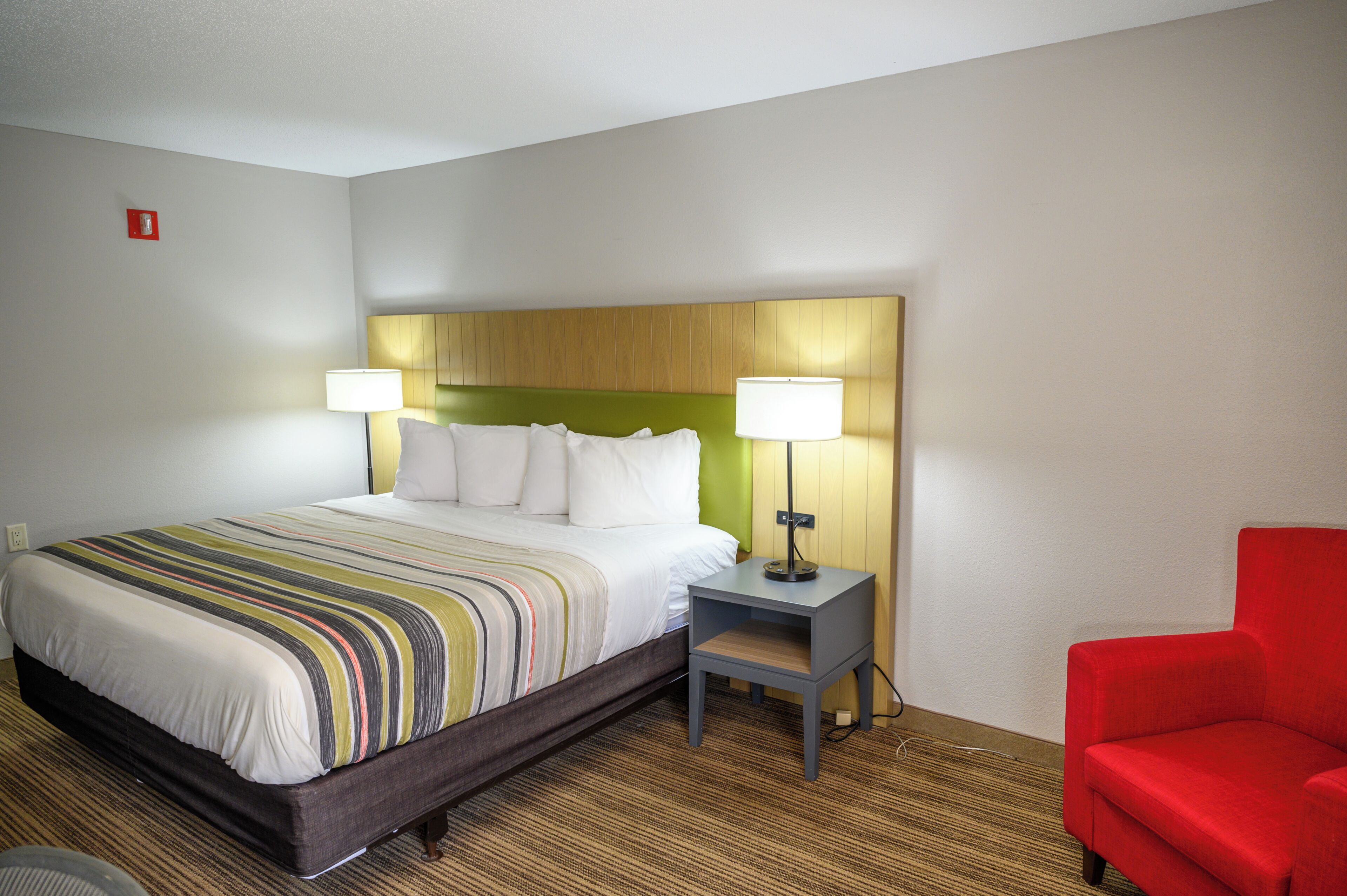Une chambre d’hôtel avec un lit, des lampes de chevet, un fauteuil rouge et une petite table.
