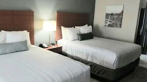 Quarto de hotel com duas camas, uma mesa de cabeceira com abajur, telefone e um quadro na parede.