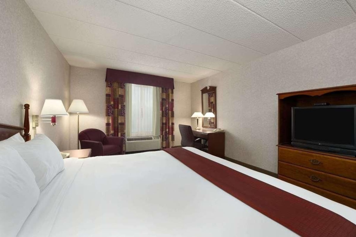 Una habitación de hotel con una cama grande, un escritorio con silla, un televisor y una ventana con cortinas.