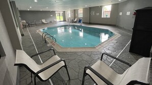 Piscina interna com água cristalina, ladeada por piso de pedra e equipada com grades de segurança.