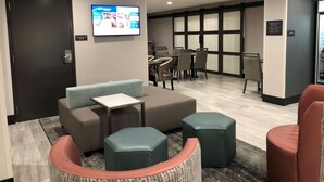 Um hall de hotel moderno com área de estar, tela de televisão e geladeira.