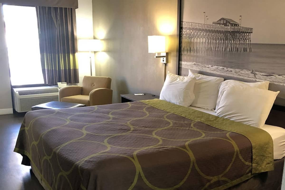 Habitación de hotel con una cama grande, una silla, un escritorio y vista a un muelle.