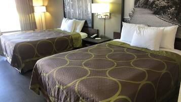 A hotel room with two beds, each with a patterned bedspread, a nightstand with a lamp, and a painting on the wall.