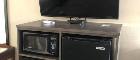 Una kitchenette compacta con microondas, refrigerador y televisor de pantalla plana montado en la pared.