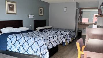 A hotel room with two beds, a wooden chair, a desk, and a large window.