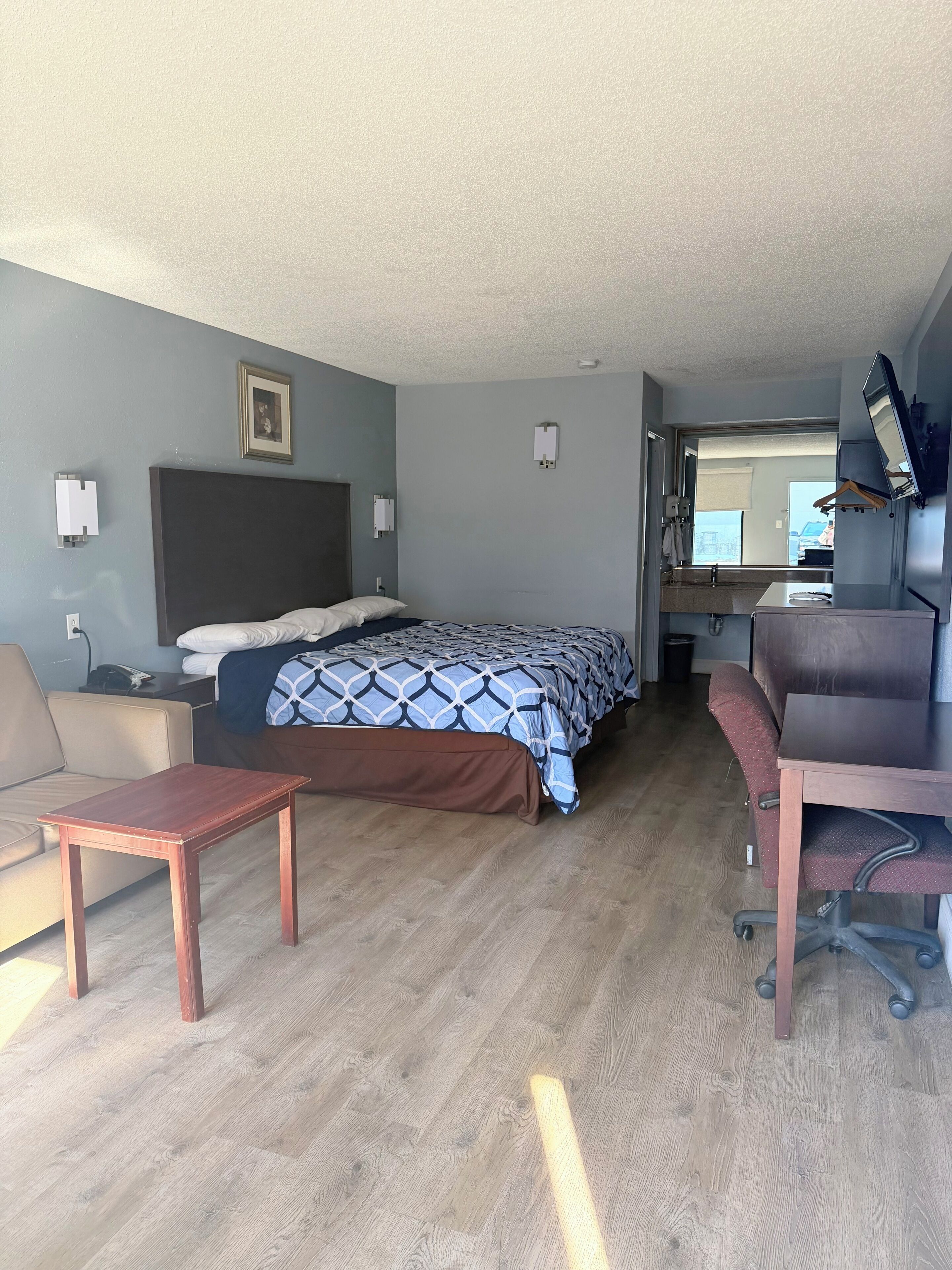 Habitación de hotel con cama, escritorio, silla, mesita y televisor.