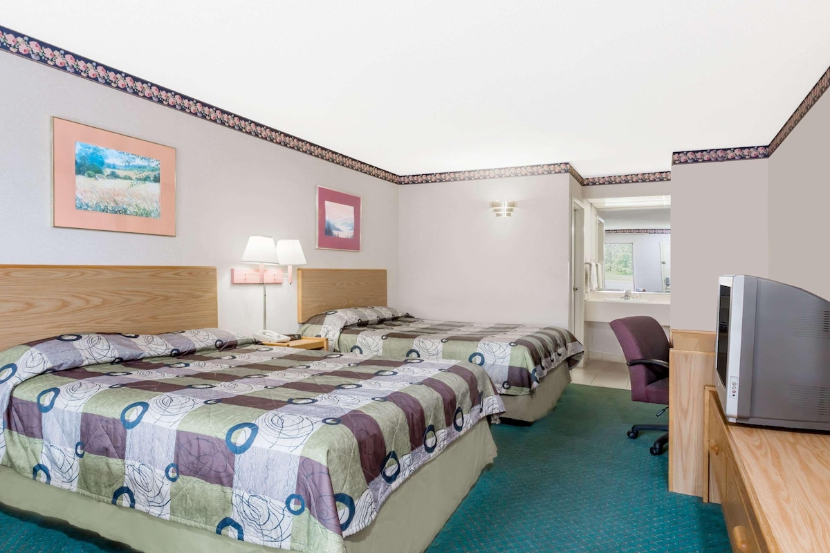 A hotel room with two beds, a desk, a chair, a television, and a bathroom visible through an open door.